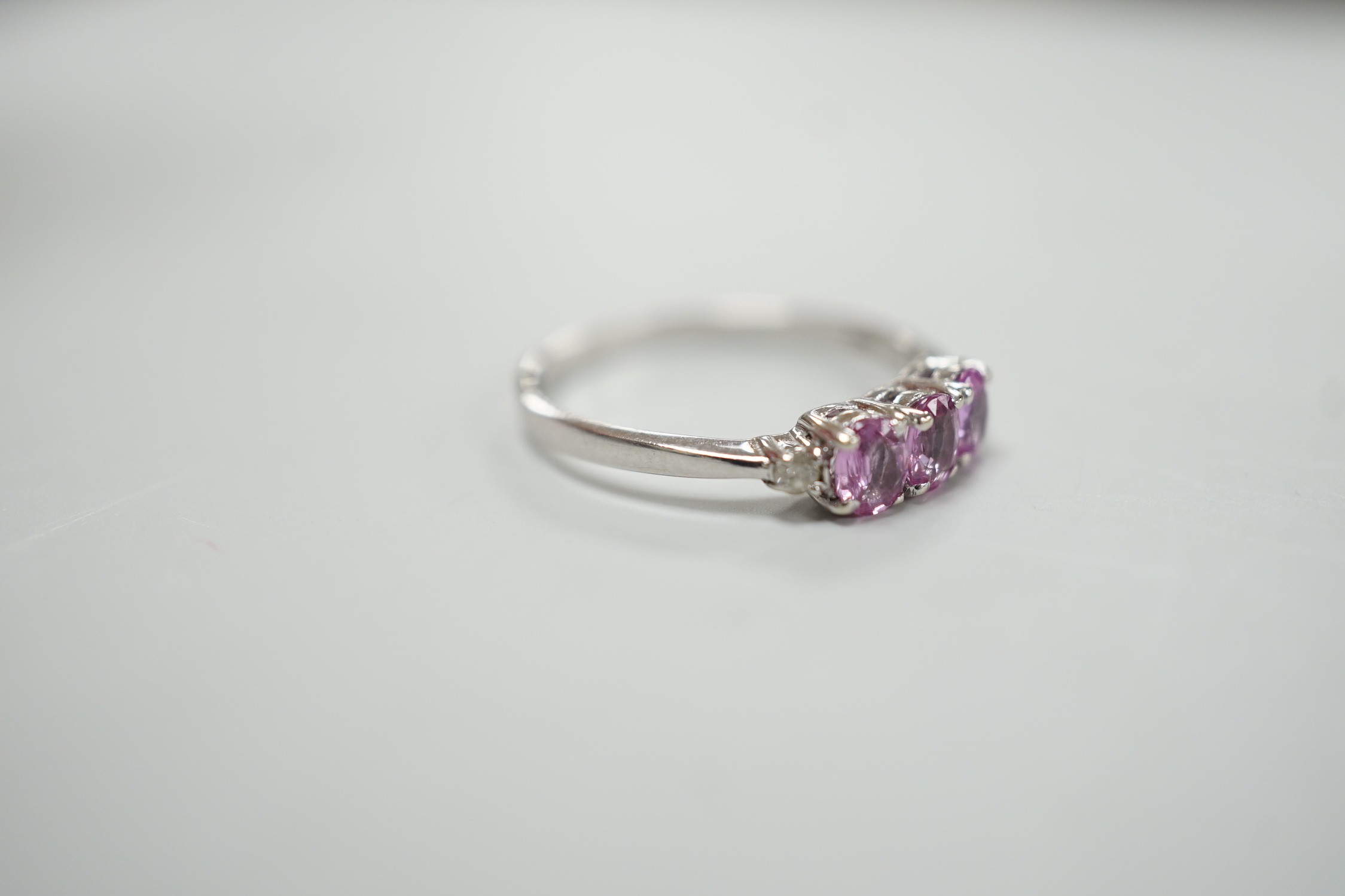 A modern 14ct white gold, three stone pink sapphire and two stone diamond chip set ring, size L, gross weight 1.5 grams.